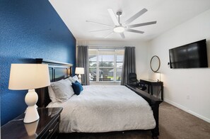 A hotel room with a bed, a desk, a chair, a TV, a ceiling fan, and a view of the outdoors through the window. - Spacious 5-bedroom house in tranquil Kissimmee with AC (Kissimmee)