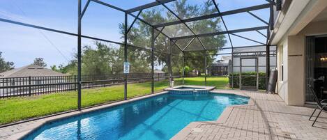 Une piscine entourée d’une structure en verre, bordée d’une terrasse en briques et d’une pelouse.