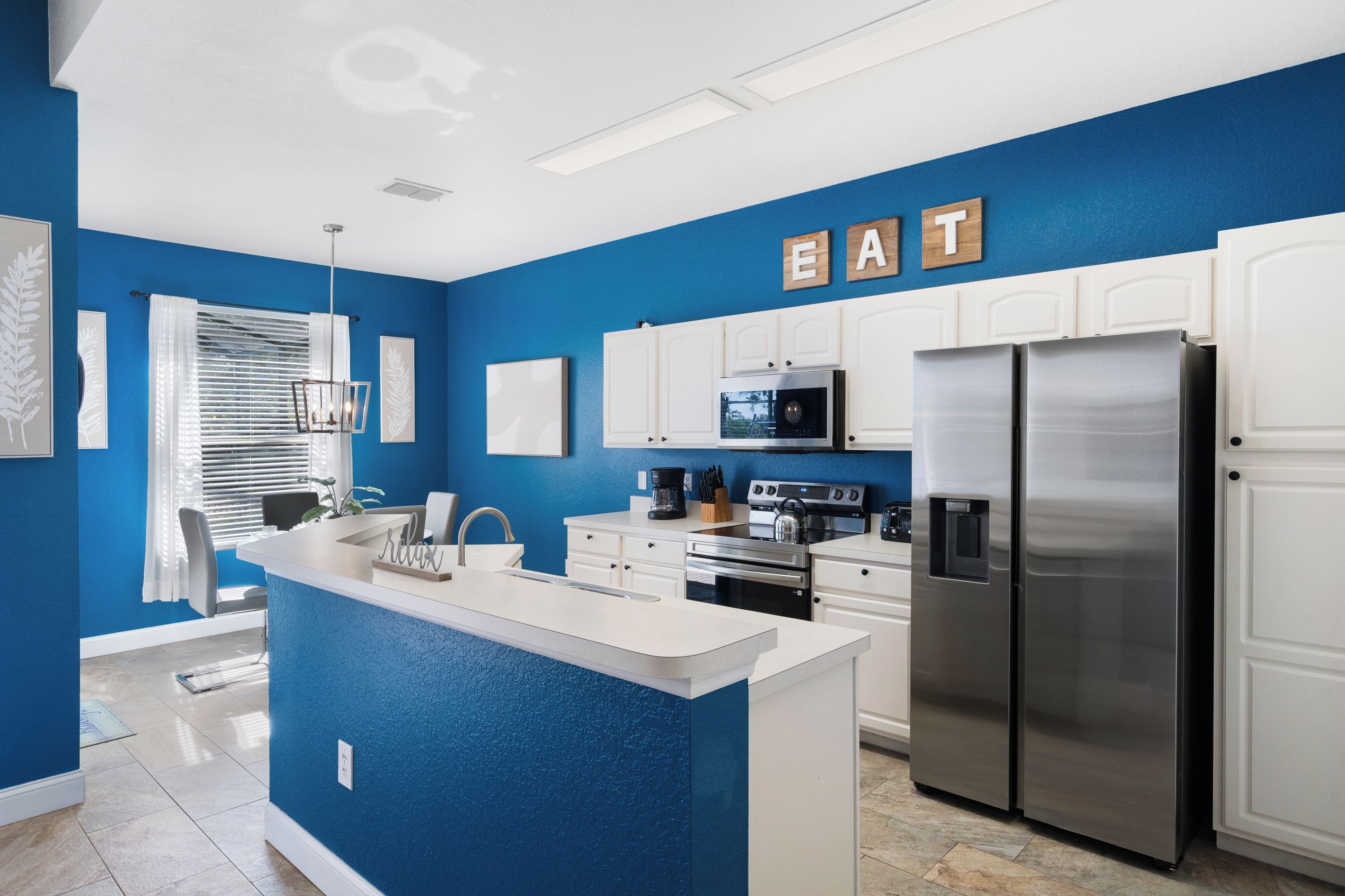 A modern kitchen with blue walls, white cabinetry, and stainless steel appliances.
