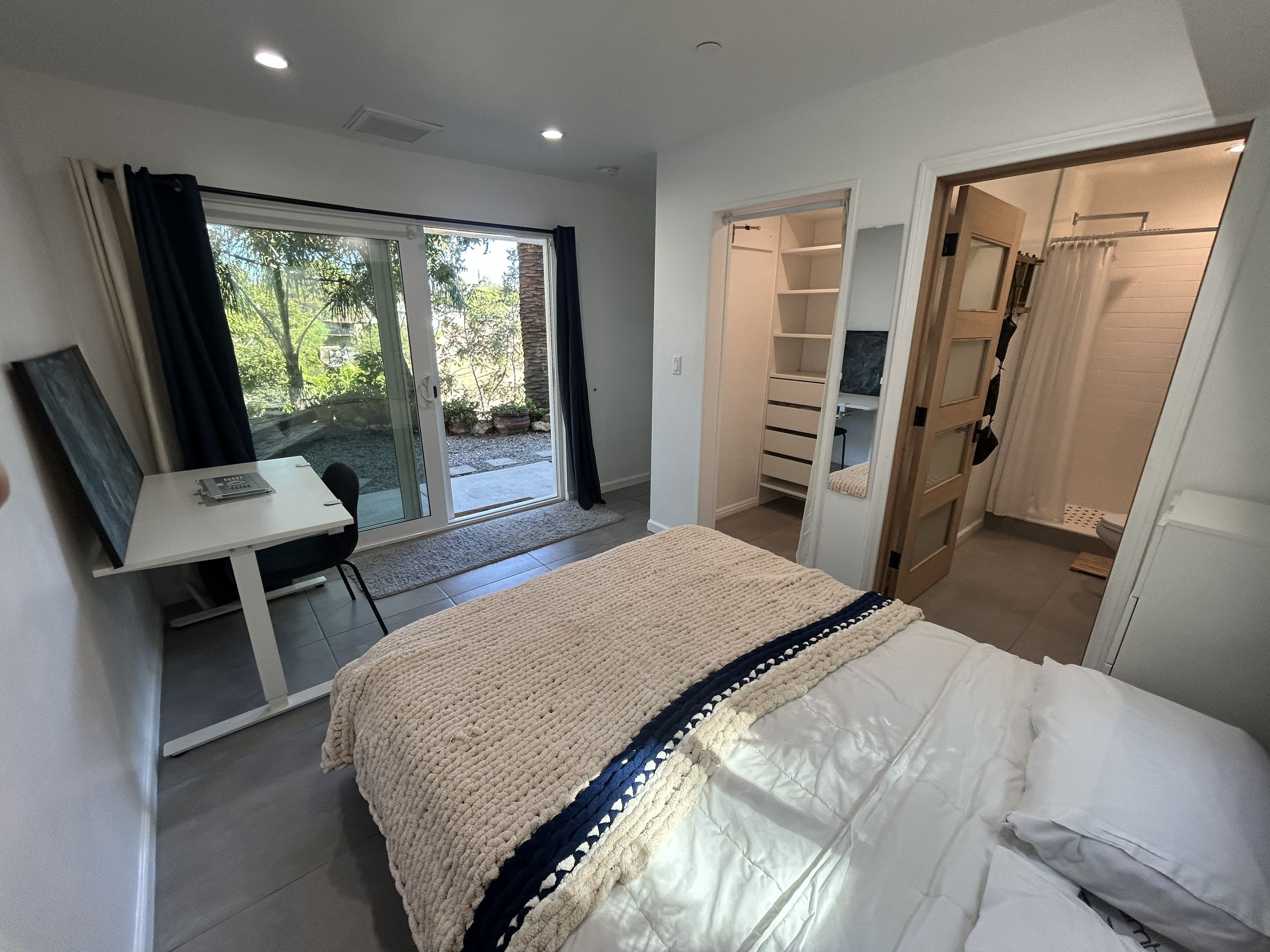 A bedroom with a bed, a desk, and a sliding door leading to a bathroom.