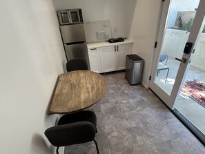 A compact kitchen with a refrigerator, microwave, and stove, a wooden dining table with two chairs, and a sliding glass door leading to an outdoor area. - Peaceful Hilltop Escape in the Heart of LA Cozy (Los Angeles)