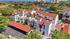 A multi-story building with a red-tiled roof, surrounded by greenery and a body of water. - Waterfront Condo Minutes to Fort Myers Beach and Sanibel Island With Pool and Spa (Fort Myers)
