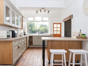 A kitchen with a large window, wooden cabinets, a built-in oven, and a countertop with stools. - Sunrise Lodge (Bridlington)