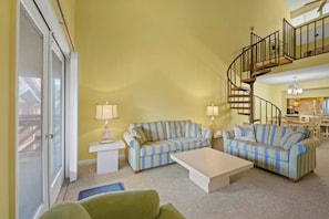 A living room with striped sofas, a coffee table, and a staircase to a second floor. - Shore Drive 3 Bedroom -Pool -Heron Pointe D16 (Myrtle Beach)