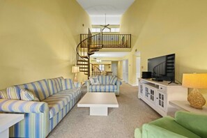 A living room with striped sofas, a flat-screen TV, a staircase, and a ceiling fan. - Shore Drive 3 Bedroom -Pool -Heron Pointe D16 (Myrtle Beach)