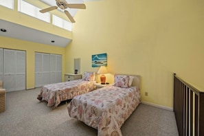 Quarto com duas camas, um ventilador de teto, mesa de cabeceira, luminária, um quadro e vista para o exterior.