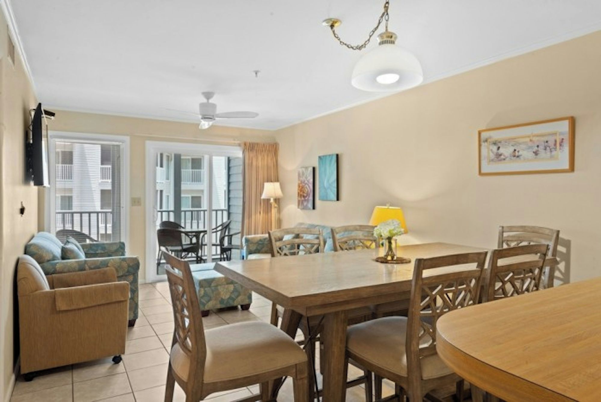 A dining area with a wooden table and chairs, a ceiling fan, and a view of the outside balcony.