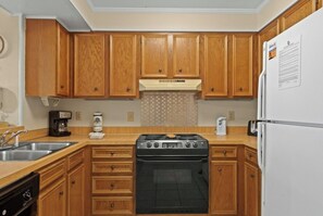 A kitchen with wooden cabinets, a stove, a refrigerator, and a coffee maker. - Pelican's Landing 208- 3BR in Shore Drive- Pool (Myrtle Beach)