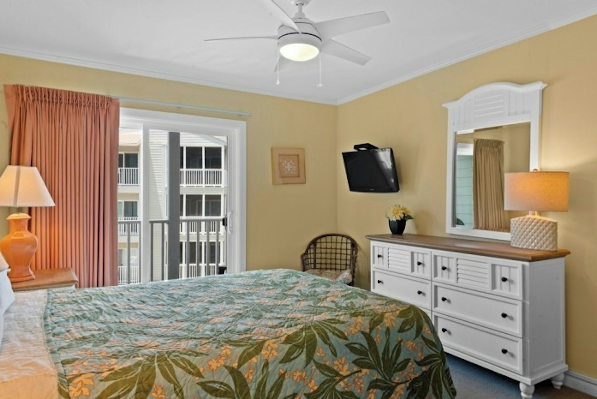 A hotel room with a bed, a dresser, a television, a ceiling fan, and a window with curtains.