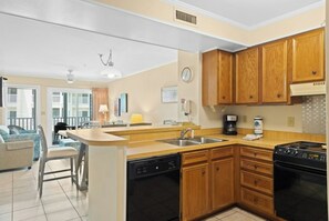A modern kitchen with wooden cabinets, a dishwasher, a stove, and a coffee maker. - Pelican's Landing 208- 3BR in Shore Drive- Pool (Myrtle Beach)