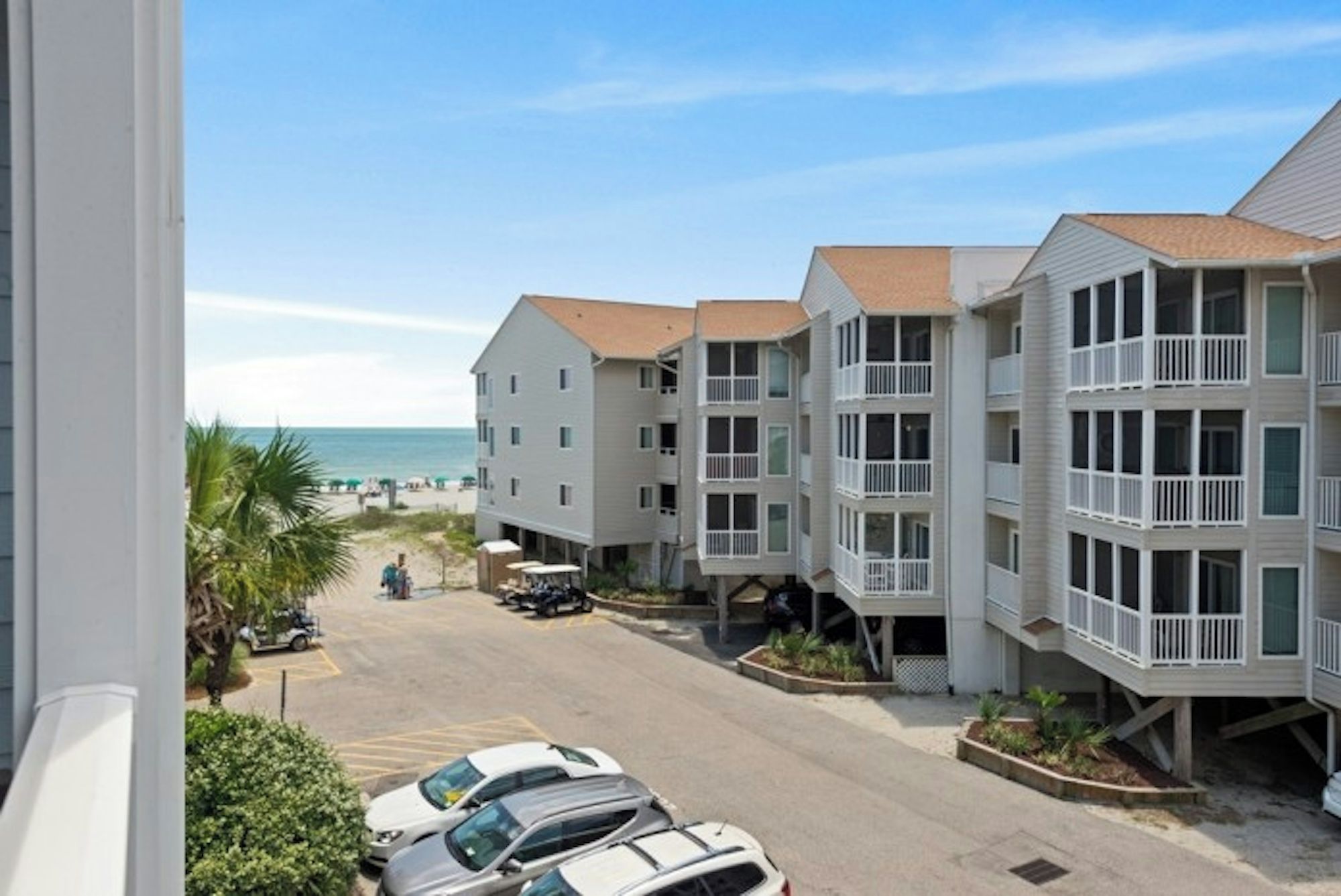 A beachfront hotel with multiple-story buildings, a parking area, and a view of the beach.
