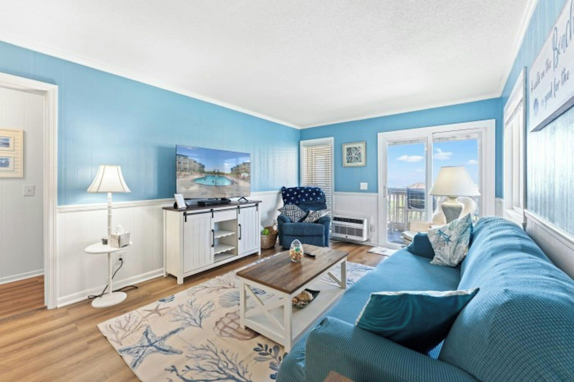 A living room with a blue sofa, a coffee table, a TV, and a view of the outdoors through a window.