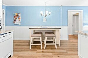 A kitchen with a dining table and two stools, a chandelier, and a bulletin board with papers. - A Place at the Beach IV 216 Oceanfront 2BR- Pool (Myrtle Beach)
