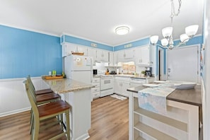 A kitchen with white cabinets, a wooden dining table, and a chandelier. - A Place at the Beach IV 216 Oceanfront 2BR- Pool (Myrtle Beach)