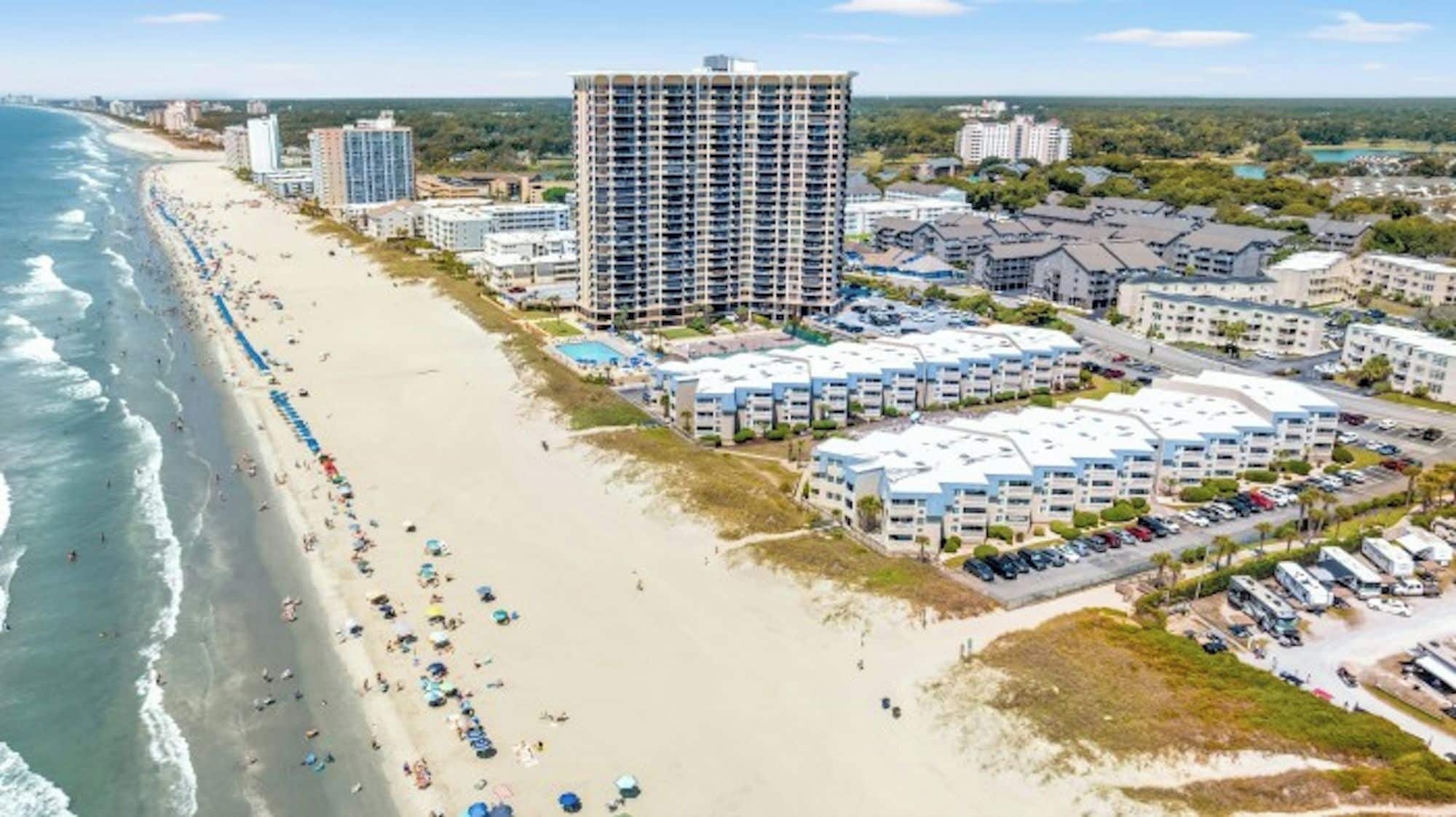 A coastal hotel with multiple buildings, a beach, and a parking area.