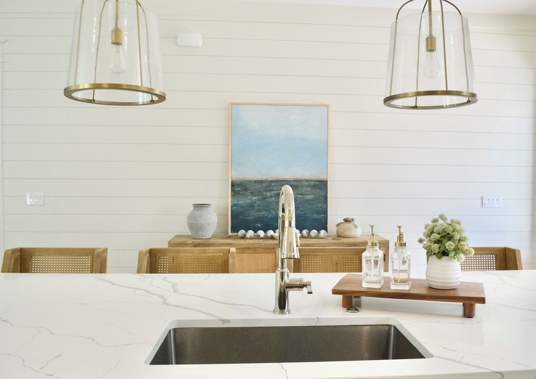 A kitchen with a marble countertop, stainless steel sink, and pendant lights.
