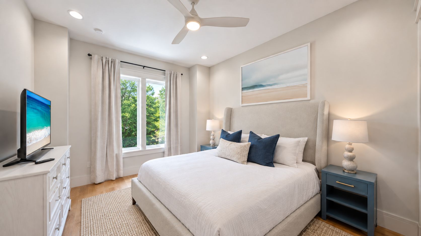 A bedroom with a bed, nightstands, a television, and a window with curtains.