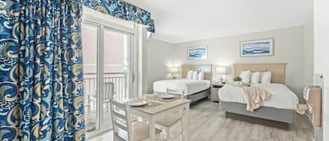 A hotel room with a balcony, two beds, a dining table, and a chair.