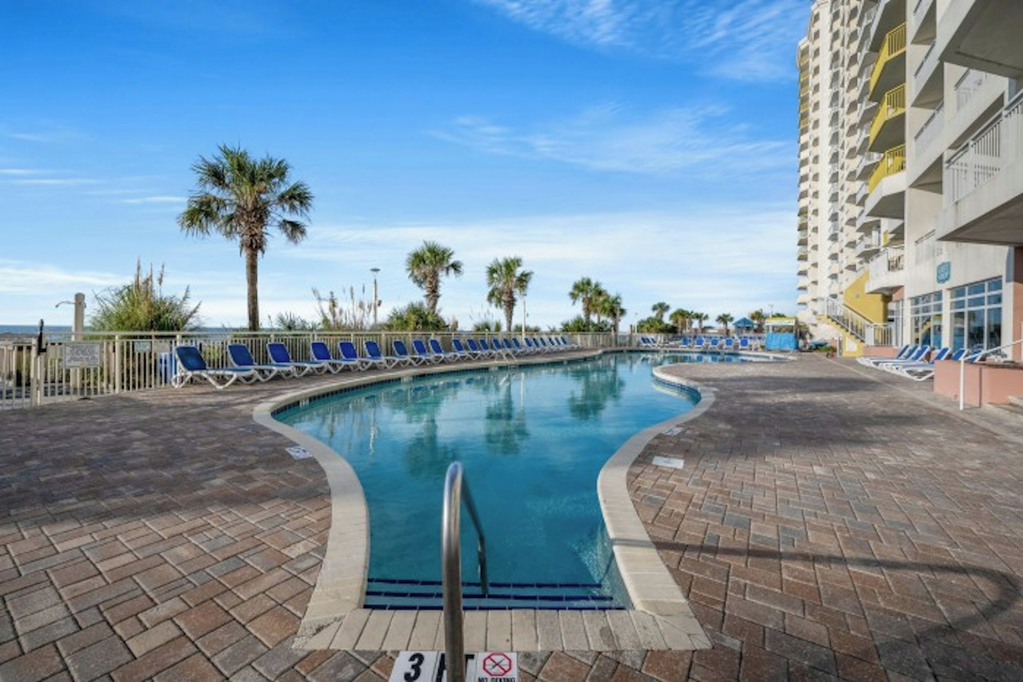 A swimming pool with lounge chairs, a no parking sign, and a tall building in the background.