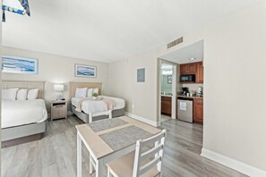 A hotel room with a bed, bedside table, lamp, and a view into the kitchen area. - Bay Watch Resort 1610 -Efficiency-Great Amenities (North Myrtle Beach)