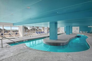 An indoor swimming pool with a tiled edge, lounge chairs, and a covered area with a view of the outside. - Oceanfront 2BR/2BA -Bay Watch 1509- Great Balcony (North Myrtle Beach)