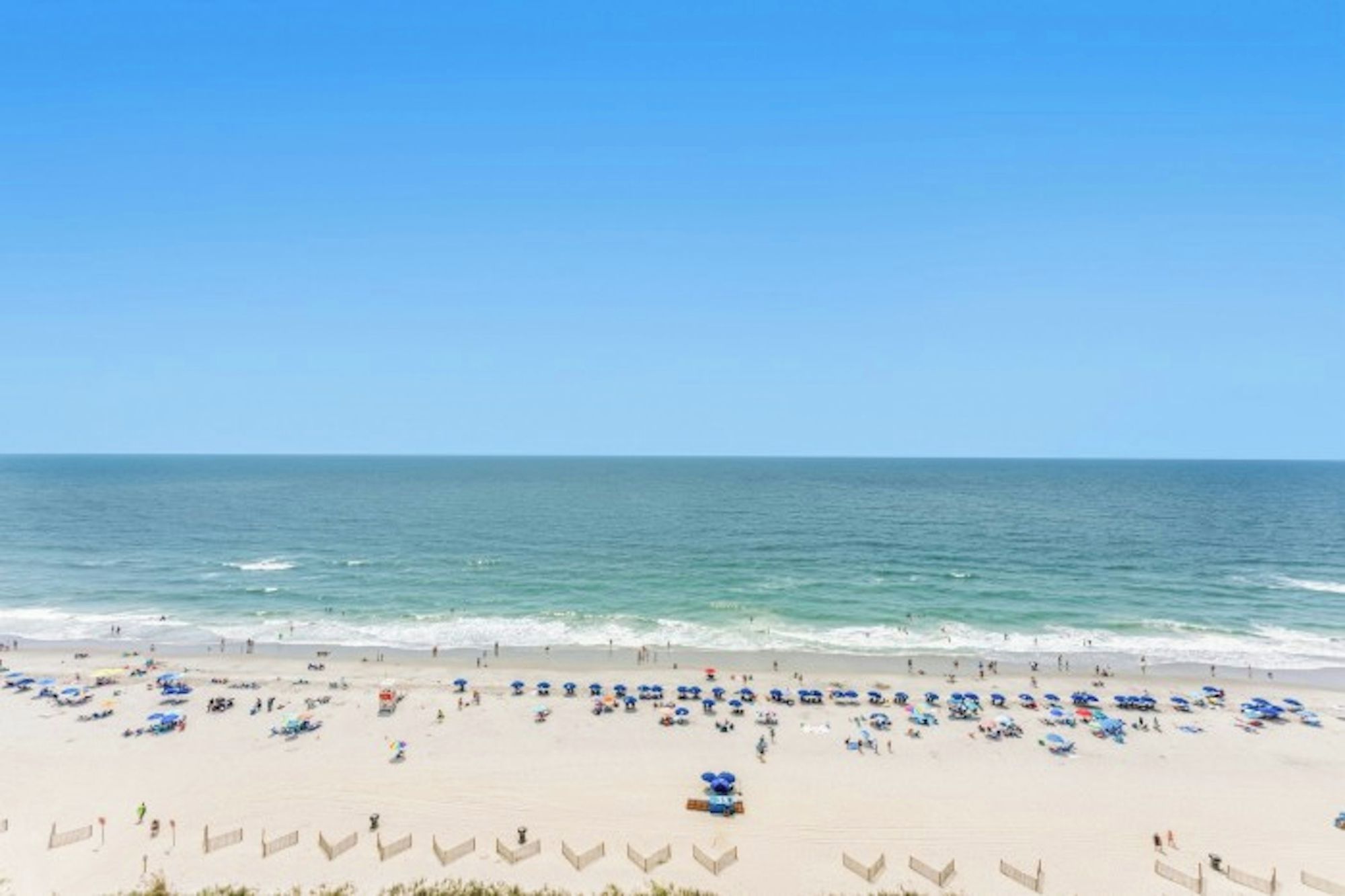Een strand met rijen parasols en ligbedden, een heldere lucht en de oceaan op de achtergrond.