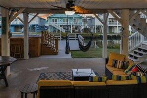 A covered outdoor area with a seating arrangement, a hammock, and a view of a building across a body of water. - Footprints in the Sand - Channel Home w/Swim Spa (North Myrtle Beach)