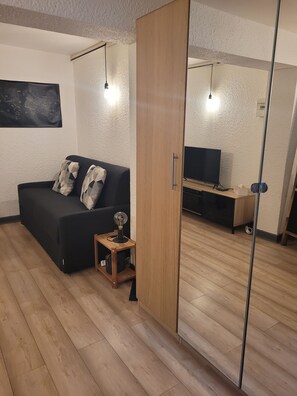A modern living room with a black sofa, a small wooden side table, and a TV stand. - Cosy studio 27, à 400m des thermes (Chamalières)