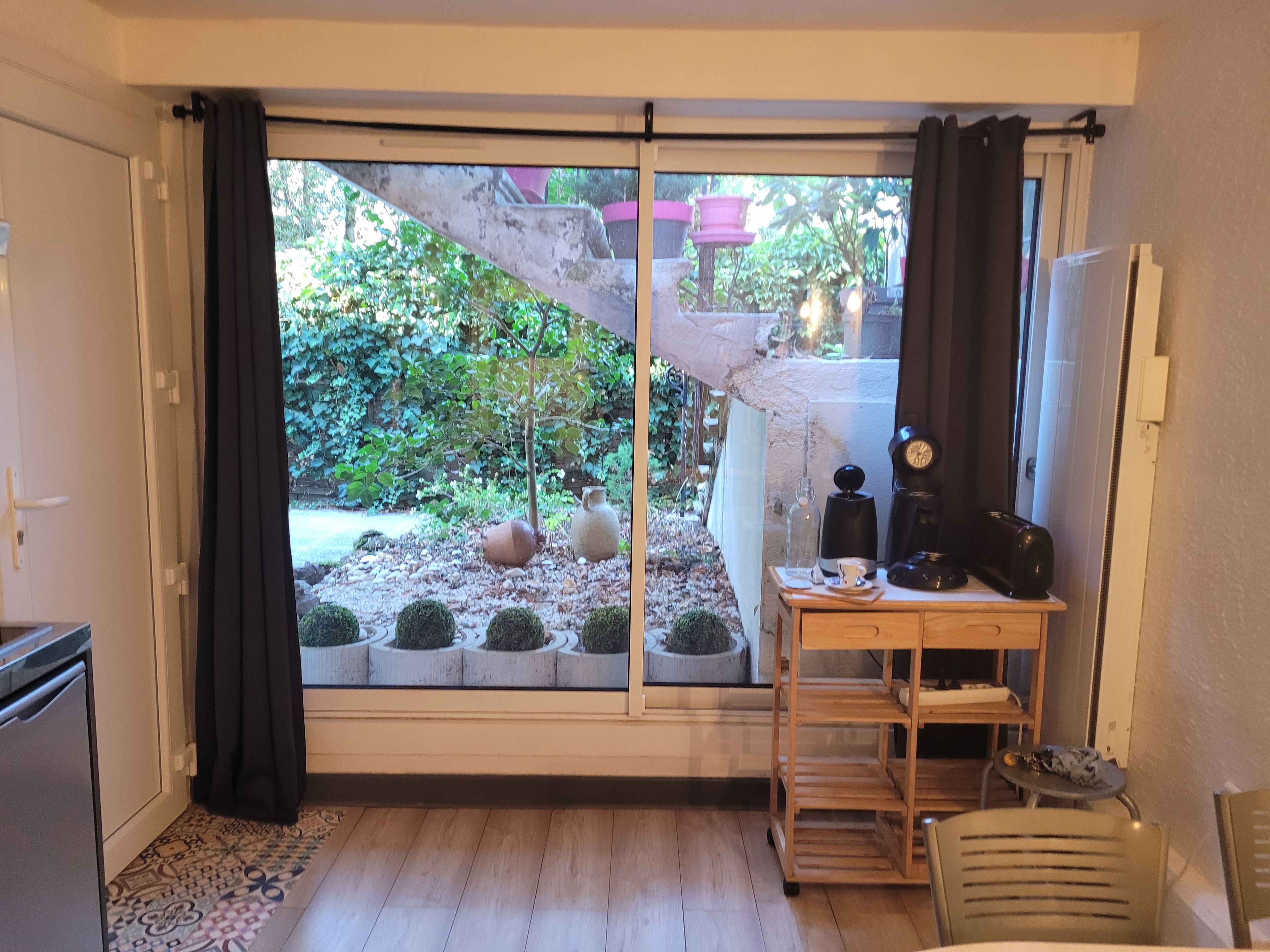 A room with a sliding glass door leading to a garden, a small table with a coffee maker, and a chair.