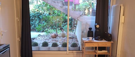 A room with a sliding glass door leading to a garden, a small table with a coffee maker, and a chair.