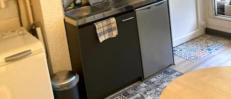 Una cocina compacta con horno integrado, un refrigerador pequeño y una cafetera. Hay una ventana con vistas a la vegetación.