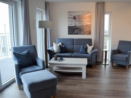 A modern living room with a grey sofa, two armchairs, a white coffee table, and a painting of a lighthouse.