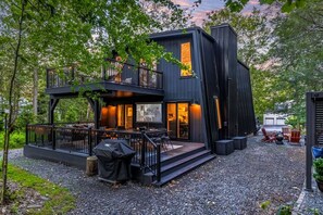 Un edificio moderno de dos pisos con balcón, mobiliario exterior y zona de parrilla.