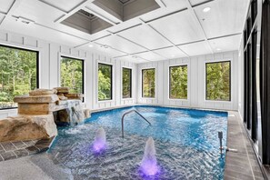 An indoor swimming pool with a waterfall feature and multiple windows. - Smoky Mountain Game Luxe Lodge (Gatlinburg)