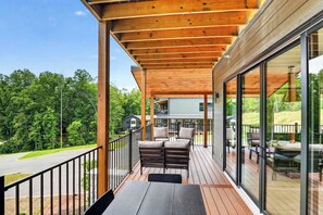 Eine Holzterrasse mit Gartenmöbeln, einer Glasreling und Blick auf eine Wohngegend.