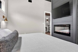 A modern hotel room with a large bed, a flat-screen TV mounted on the wall, and a built-in fireplace. - Smoky Mountain Game Luxe Lodge (Gatlinburg)
