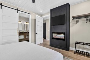 A modern bedroom with a bed, a fireplace, a wardrobe, and a bathroom visible through an open door. - Smoky Mountain Game Luxe Lodge (Gatlinburg)