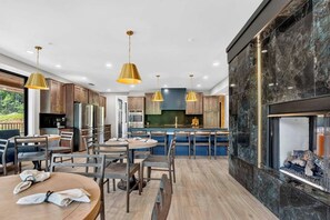 A modern kitchen with a central island, pendant lighting, and a stone fireplace. - Smoky Mountain Game Luxe Lodge (Gatlinburg)