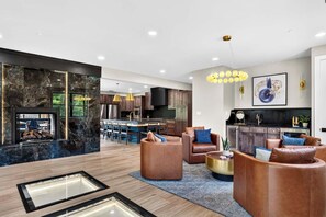 A modern living room with leather sofas, a fireplace, and a kitchen in the background. - Smoky Mountain Game Luxe Lodge (Gatlinburg)