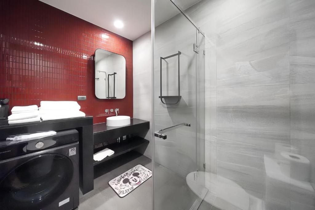 Ein modernes Badezimmer mit rotem Fliesenbelag an der Wand, einem schwarzen Waschbecken, einem Spiegel, einer Duschkabine aus Glas und einer schwarzen Waschmaschine.