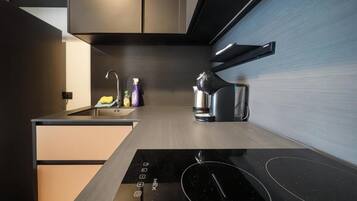 A modern kitchen with a built-in induction cooktop, a stainless steel sink, and a kettle.