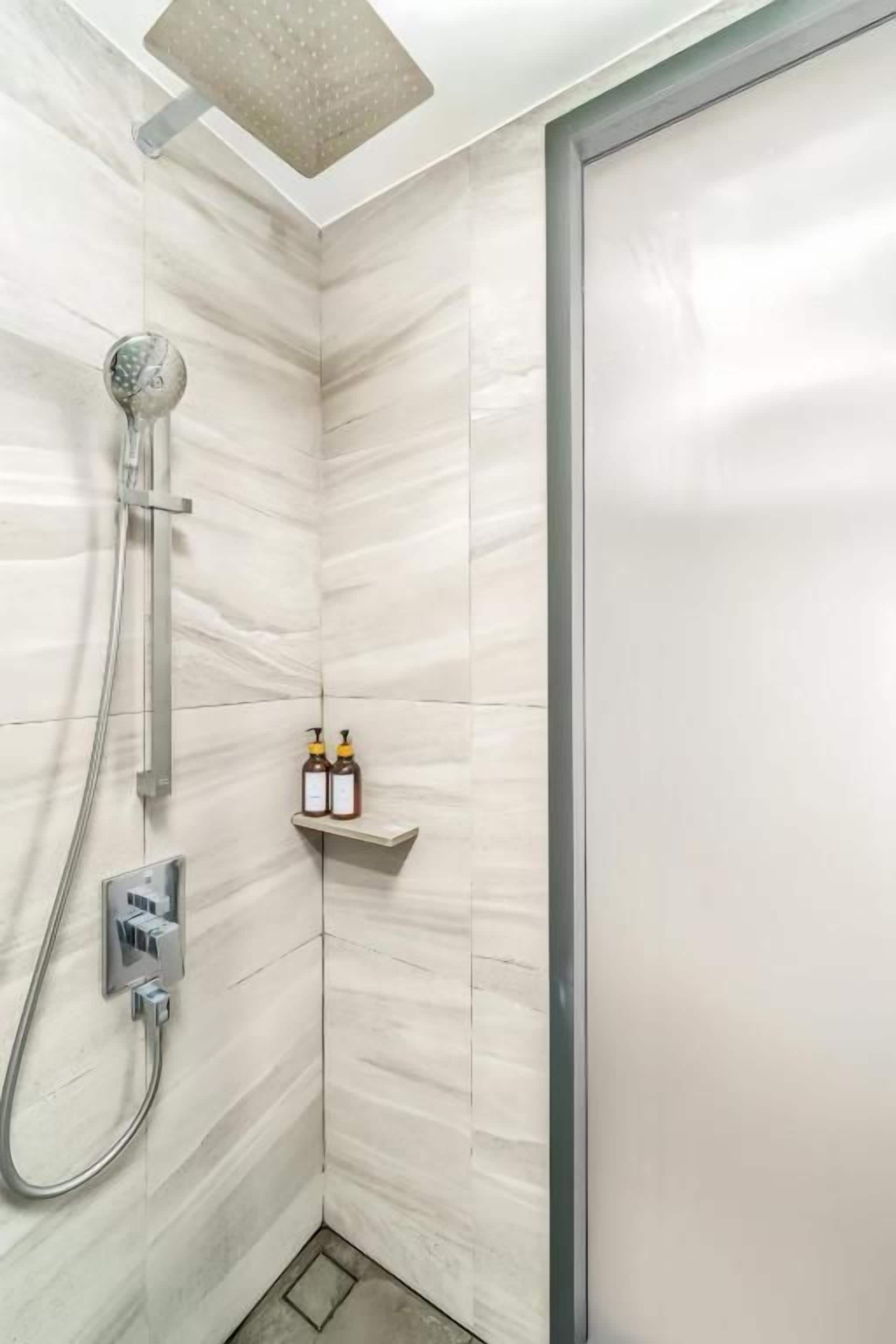A shower area with a handheld showerhead, a wall-mounted faucet, and a shelf with two bottles.