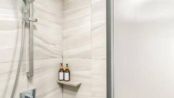 A shower area with a handheld showerhead, a wall-mounted faucet, and a shelf with two bottles.