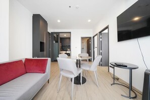 A modern living room with a sofa, a dining table with chairs, a TV mounted on the wall, and a kitchen area in the background. - Edge Central Pattaya (Pattaya City)