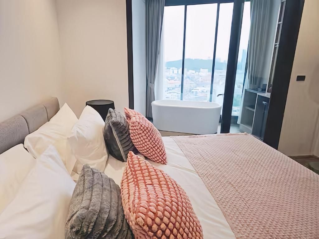 Ein Schlafzimmer mit einem großen Bett, Blick auf eine Stadtlandschaft durch ein Fenster und einer Badewanne in der Ecke.