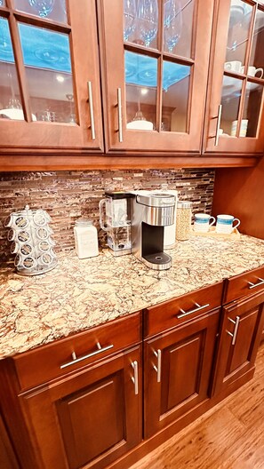 A kitchen with wooden cabinets, a coffee maker, a glass carafe, and a decorative bottle holder. - Cozy Retreat On The Eastside Estate (sleep14) (Greater Napanee)