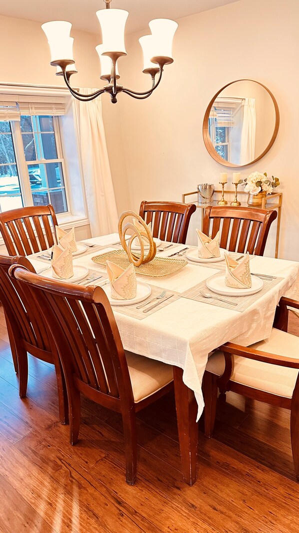 Comedor con una mesa redonda dispuesta para seis comensales, sillas de madera, una araña y un espejo en la pared.