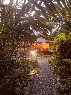 A pathway leading to a building with a wooden deck and a warm light source. - Casa Caribeña (Limón)