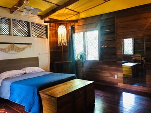 A wooden room with a bed, a bench, a fan, and a window. - Casa Caribeña (Limón)