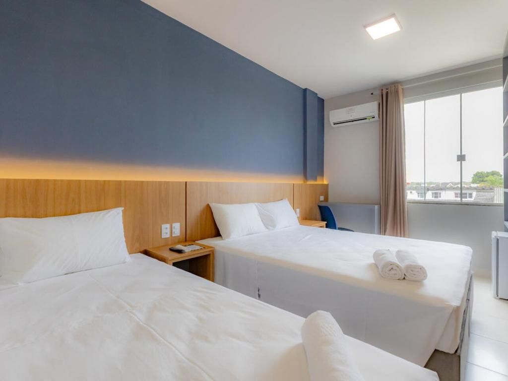 Quarto de hotel com duas camas, cabeceira de madeira, janela com vista e ar condicionado.